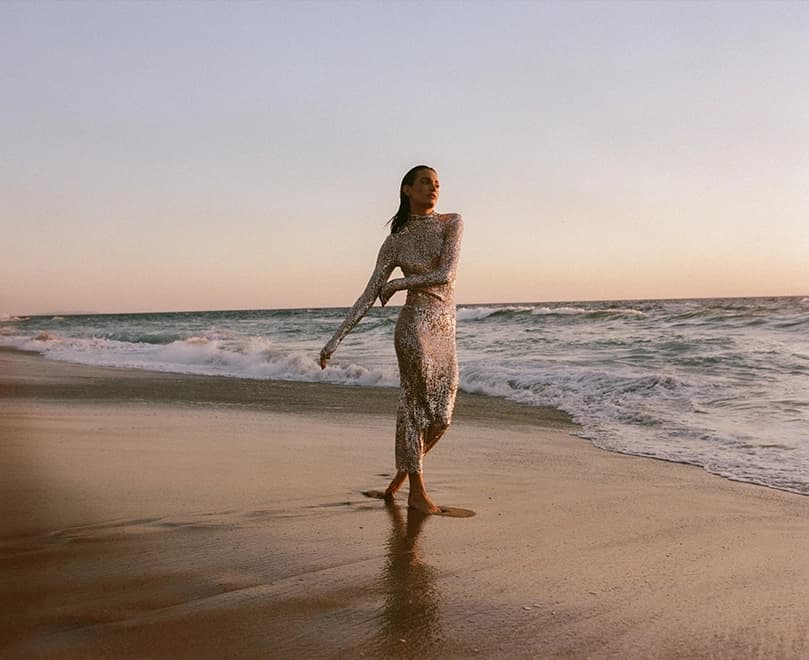 woman wearing a full length dresswalking on the beach at sunset